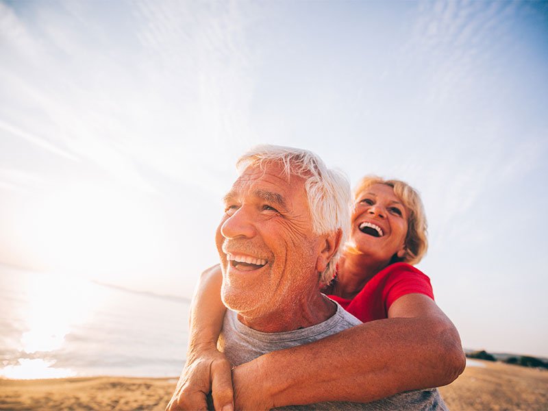 Active, well-aged couple - laughing man carrying joyful woman outdoors